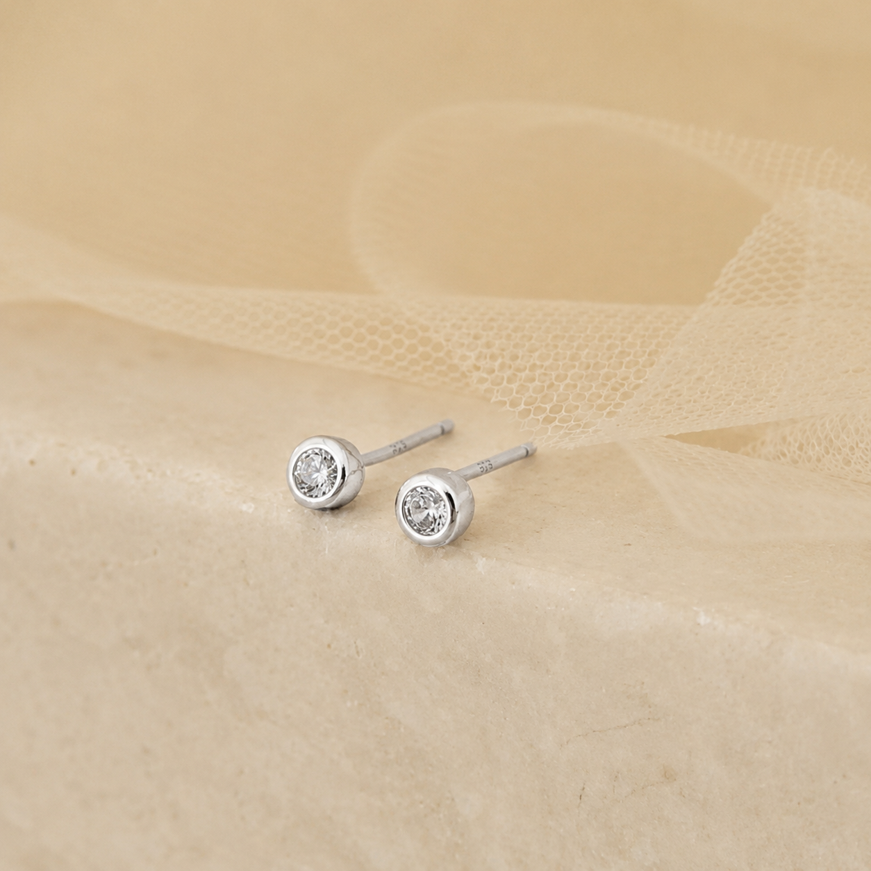 Pair of silver stud earrings with clear gemstones on a beige fabric background